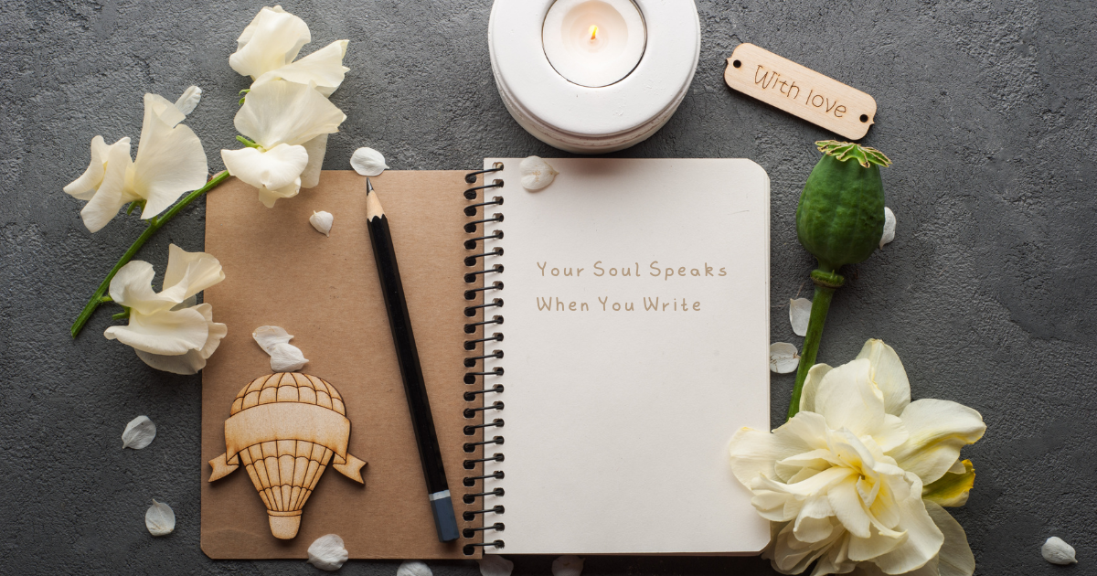 Flat lay of a journal with the words “Your Soul Speaks When You Write,” a pencil, white flowers, a lit candle, and a wooden tag reading “With love,” symbolizing self-care, reflection, and emotional healing through writing.